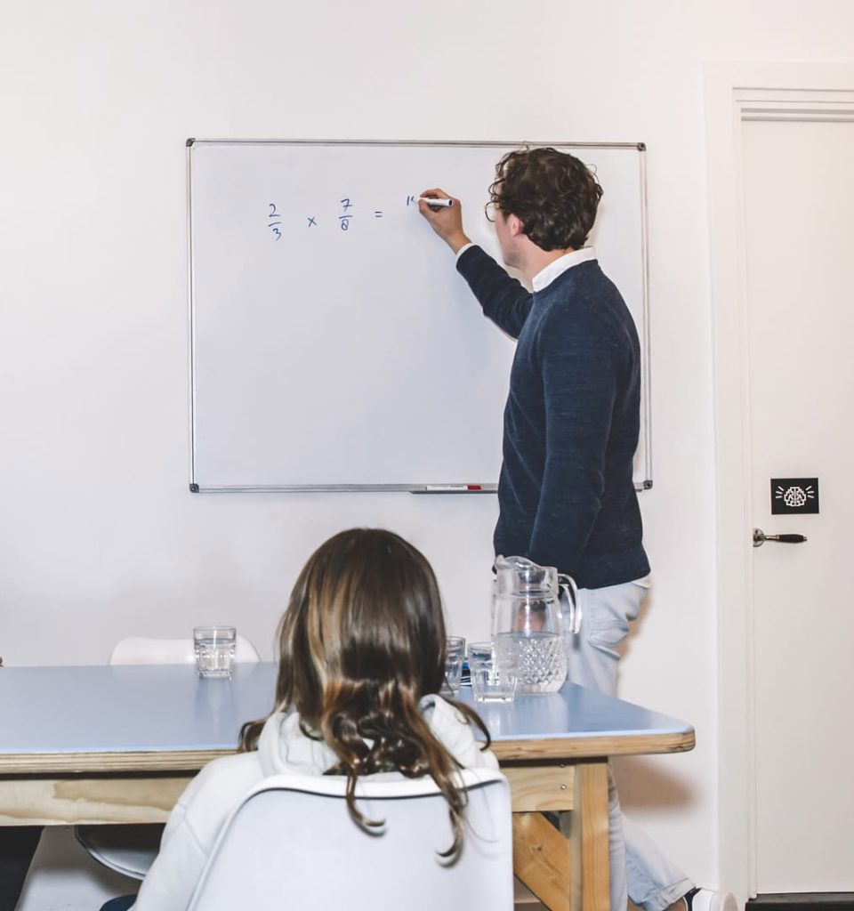 Docent schrijft wiskunde breuken op whiteboard terwijl leerling toekijkt bij Brainboost bijles